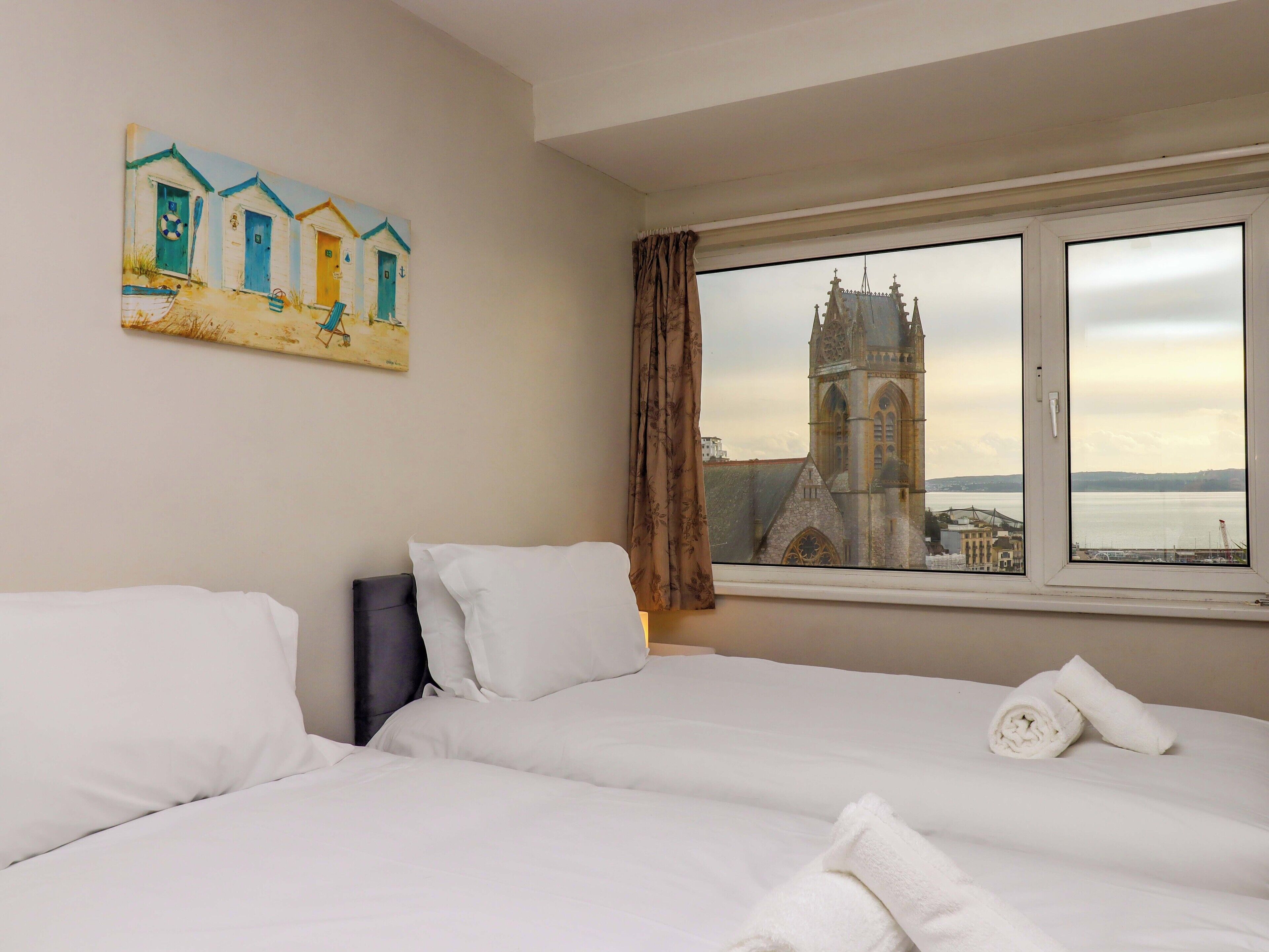 Ein Hotelzimmer mit einem großen Bett, einem Bild von Strandhütten und Blick auf eine Kirche und Wasser.