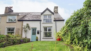 A two-story house with a white exterior, a blue door, and a well-maintained garden with various plants and a lawn.