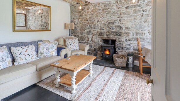 A cozy living room with a stone wall, a fireplace, a sofa with patterned cushions, and a wooden coffee table.