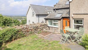 A house with a stone wall, a wooden door, and a garden with a table and chairs.