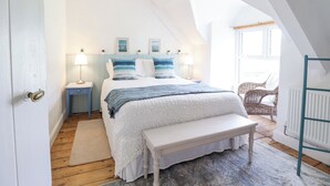 A bedroom with a bed, bedside tables, a bench, a chair, and a window.