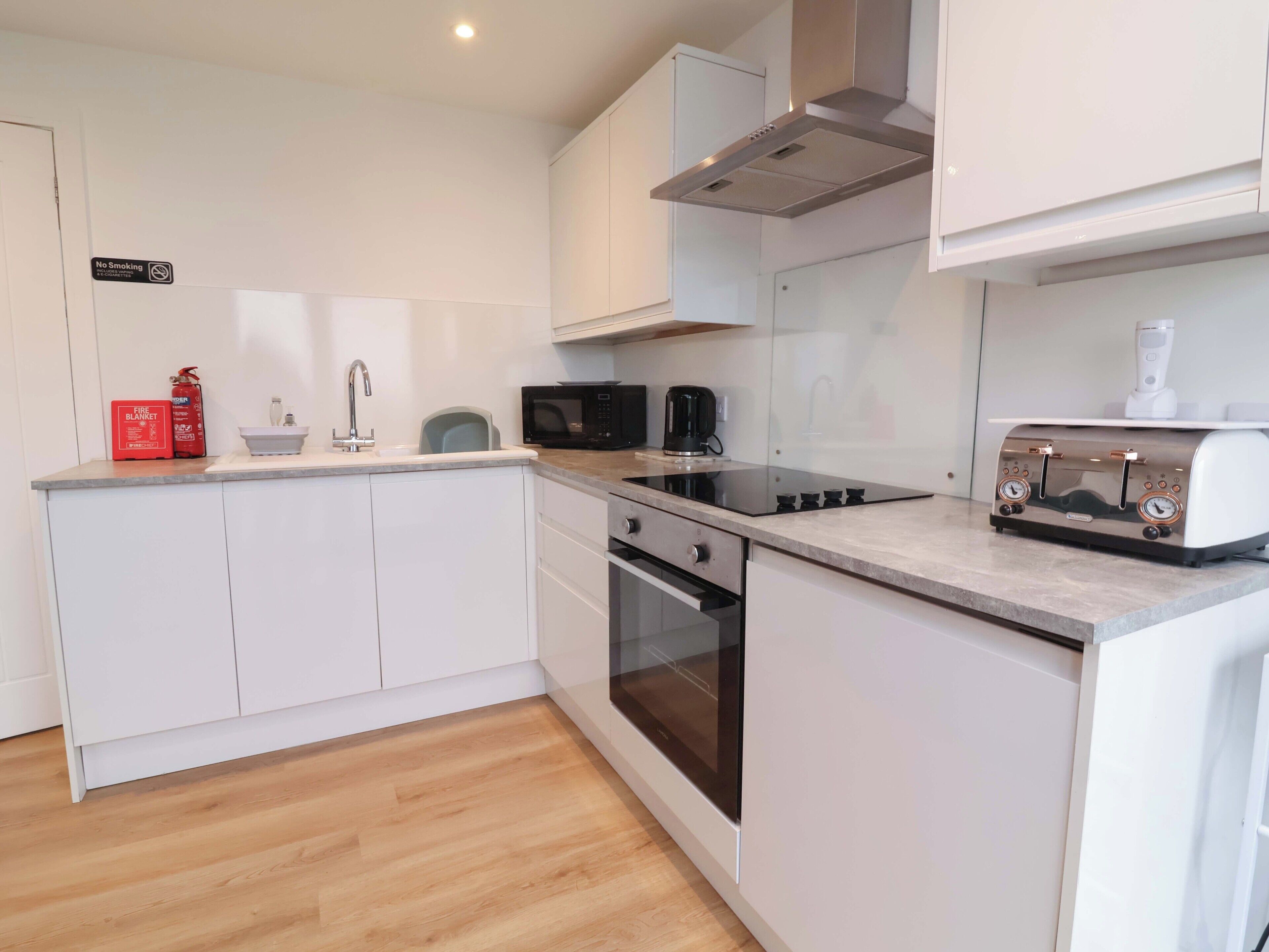 A modern kitchen with white cabinets, a stainless steel range hood, a microwave, a toaster, and a fire extinguisher.