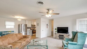 A living room with a beige sofa, patterned cushions, a glass coffee table, a teal armchair, a ceiling fan, and a flat-screen TV. - Near Hunting Grounds: Quiet Home in Aspermont! (Aspermont)