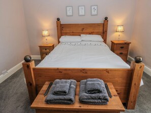 Ein hölzernes Bett mit weißen Leinen, zwei Nachttische mit Lampen sowie eine Bank mit gefalteten Handtüchern.