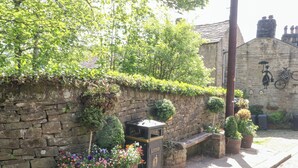 A stone wall with a bench, potted plants, and a 'LITTER' sign. - Penny Cottage (Keighley)