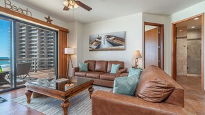 A living room with a leather sofa, a coffee table, and a painting of boats on water. - Las Palomas Phase II Coronado 503 Exceptional OceanFront 3BR 2BA Unit. (Puerto Peñasco)