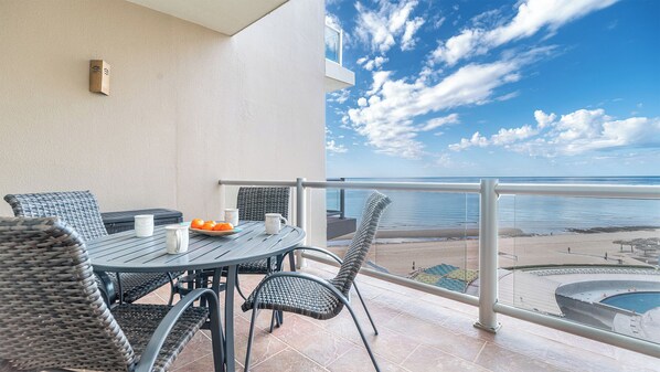 Un balcon avec une table et des chaises, une vue sur la plage et une piscine.