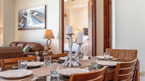 A dining area with a table set for four, a brown leather sofa, a painting on the wall, and a lamp on the table. - Las Palomas Phase II Coronado 503 Exceptional OceanFront 3BR 2BA Unit. (Puerto Peñasco)