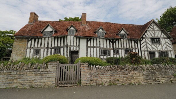 A Tudor-style building with a stone wall and a wooden gate.