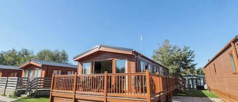 A wooden cabin with a balcony, a paved driveway, and a grassy area.