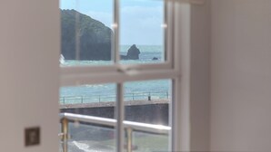 A view through a window of a coastal scene with a rocky outcrop and a pier. - Demelza (Helston)