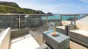 A balcony with wicker furniture and a glass railing overlooking a coastal landscape. - Demelza (Helston)