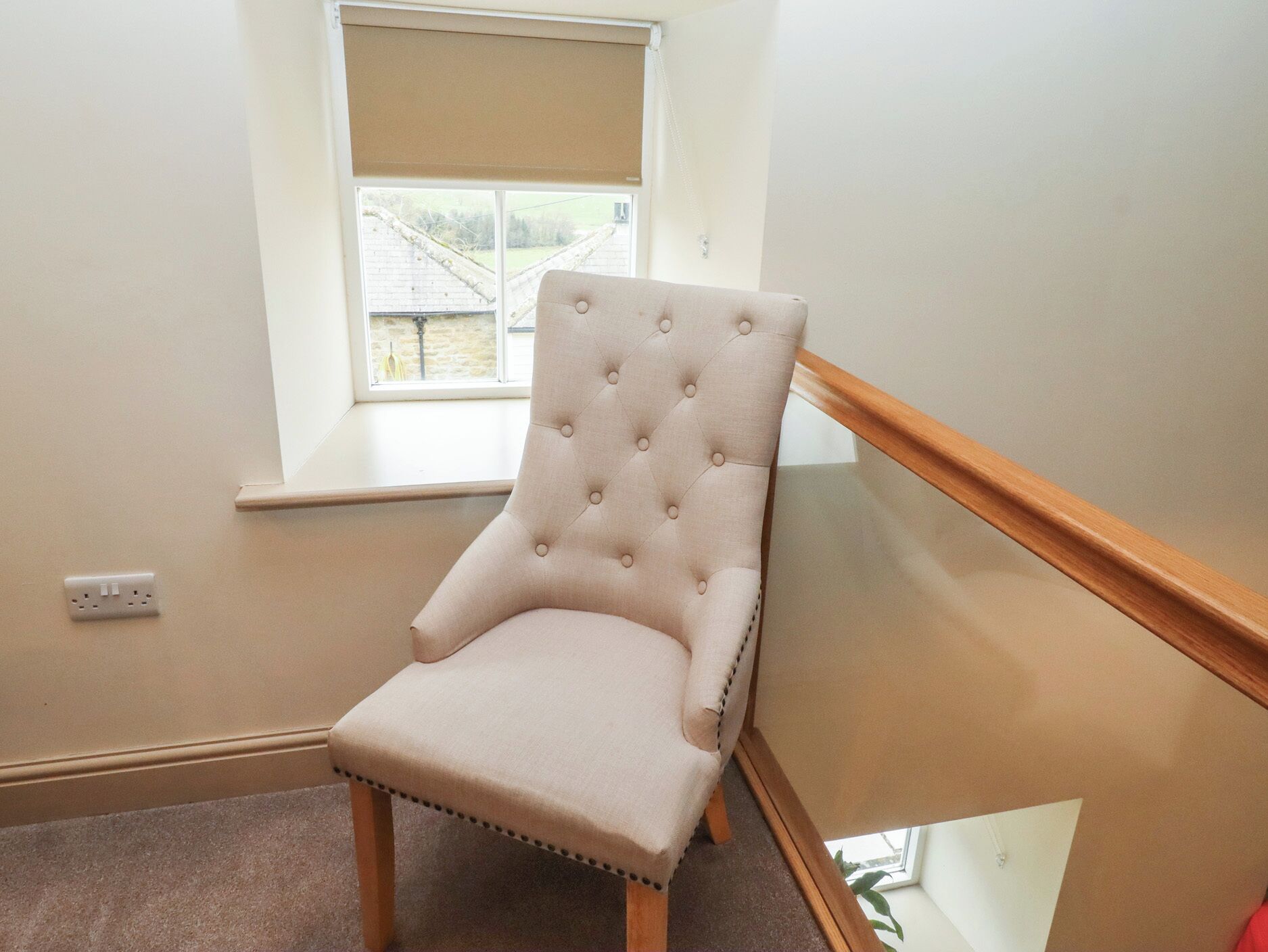 A chair in a corner with a window, a power outlet, and a wooden floor.