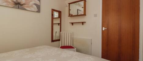 A bedroom with a bed, a wooden door, a radiator, a mirror, and a floral wall decoration.