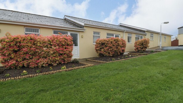 A row of single-story houses with a uniform exterior design, featuring a flat roof and a small front yard with a well-maintained lawn and flowering bushes. - Blorenge (Abergavenny)