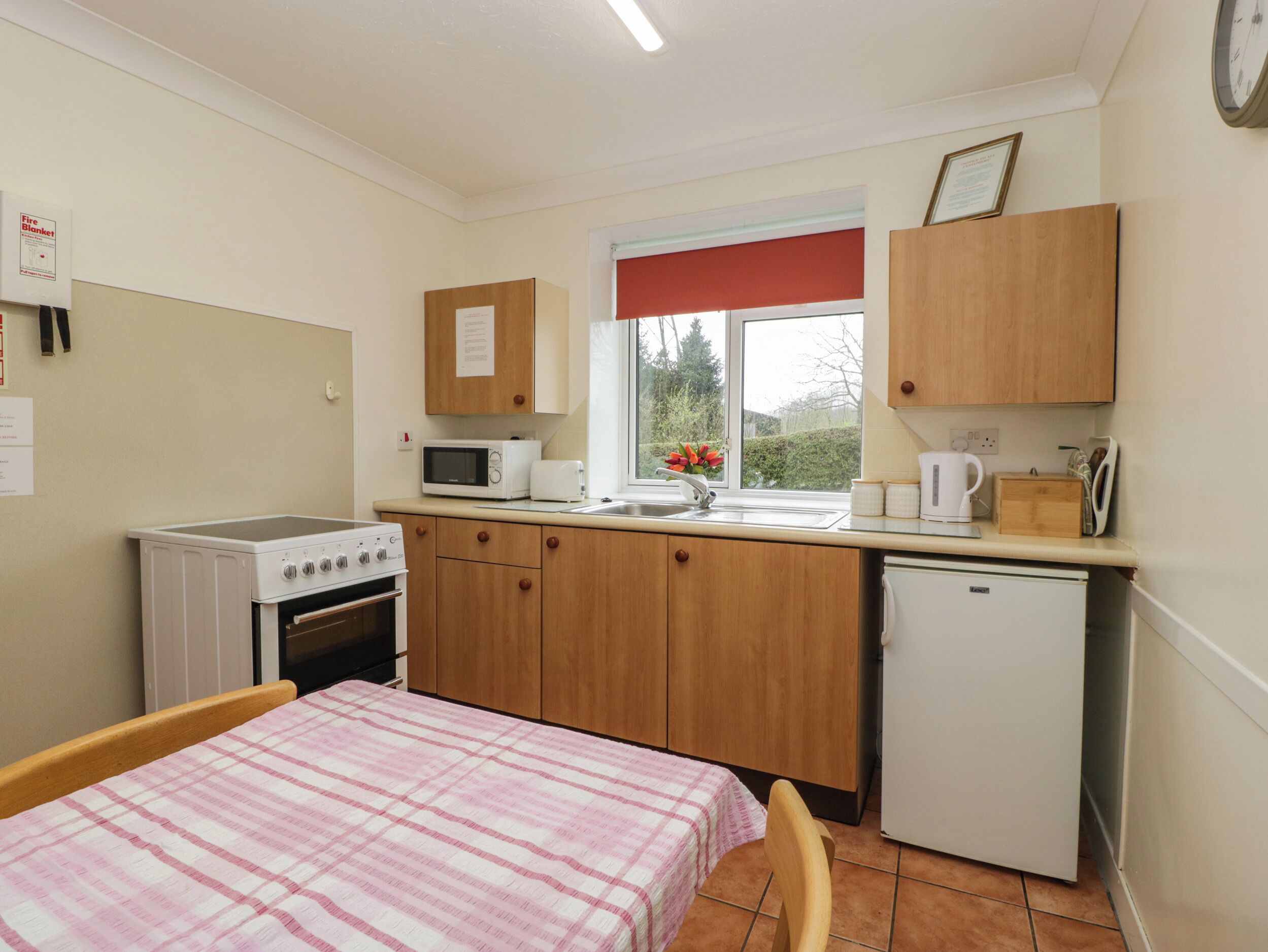 A compact kitchen with a microwave, toaster, and sink. There's a small refrigerator, a stove, and a window with a view of greenery.