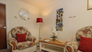 A living room with two floral armchairs, a wooden coffee table, a red floor lamp, a wall clock, and a bulletin board with various items pinned to it. - Blorenge (Abergavenny)