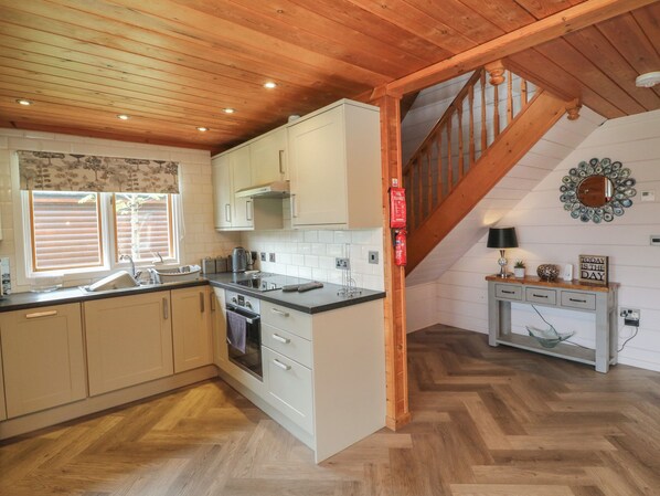 A kitchen with wooden ceiling beams, white cabinets, a herringbone floor, a built-in oven, and a staircase leading to another level. - Cedar (Winkleigh)