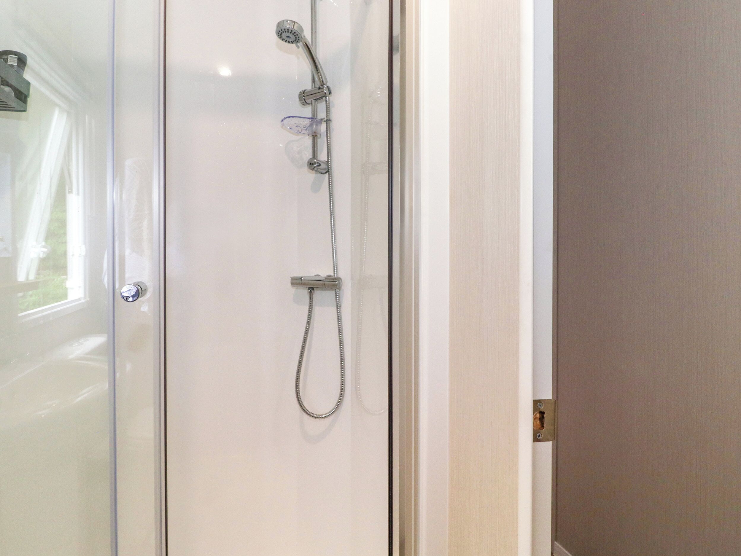 A glass shower enclosure with a handheld showerhead and a handheld shower attachment.