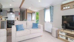 A compact living space with a kitchenette, a sofa, a TV, and a sign reading "CARAVAN LIFE". - Elton's Escape (Windermere)