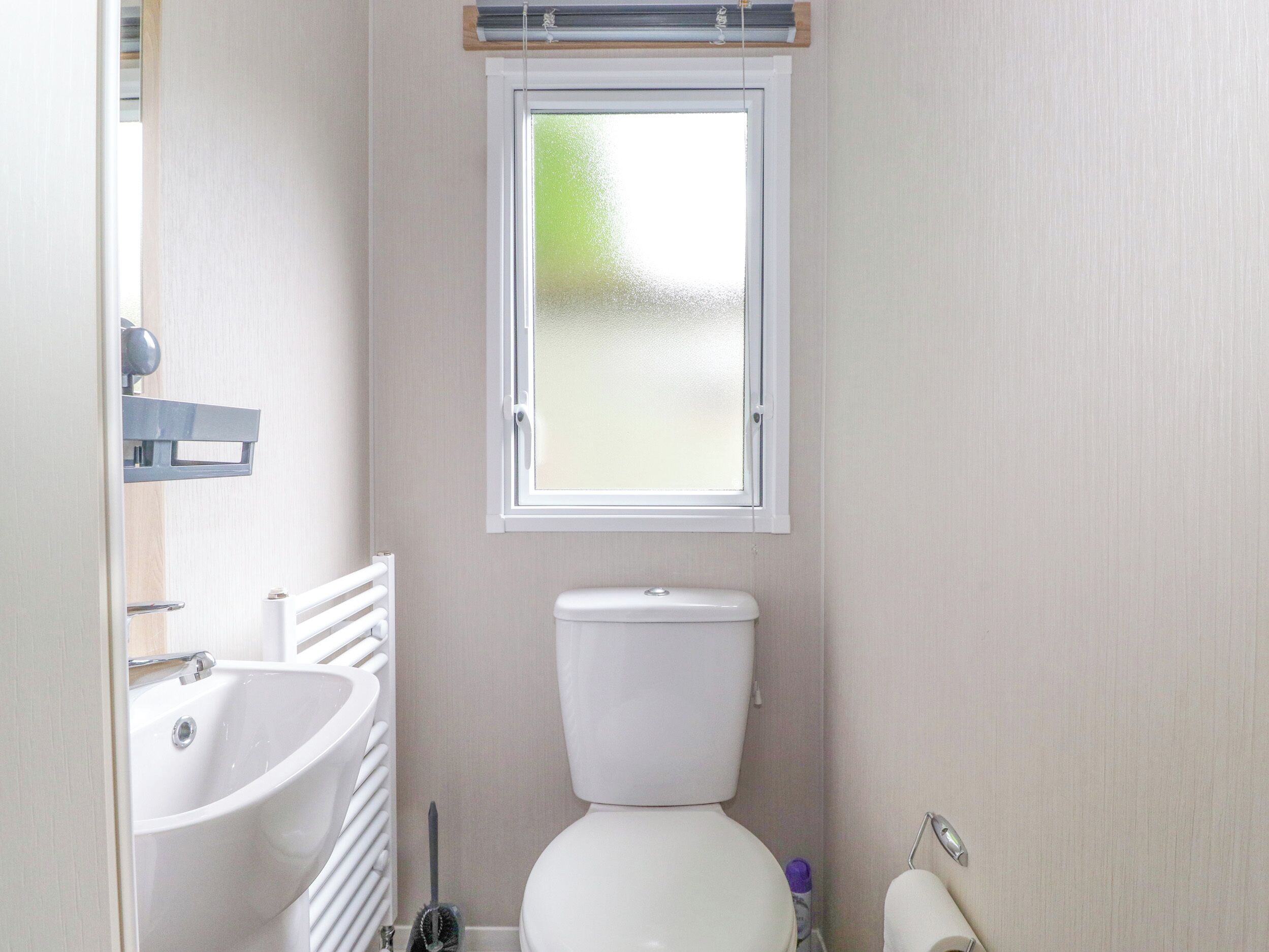 Et lille badeværelse med toilet, vask og et vindue.