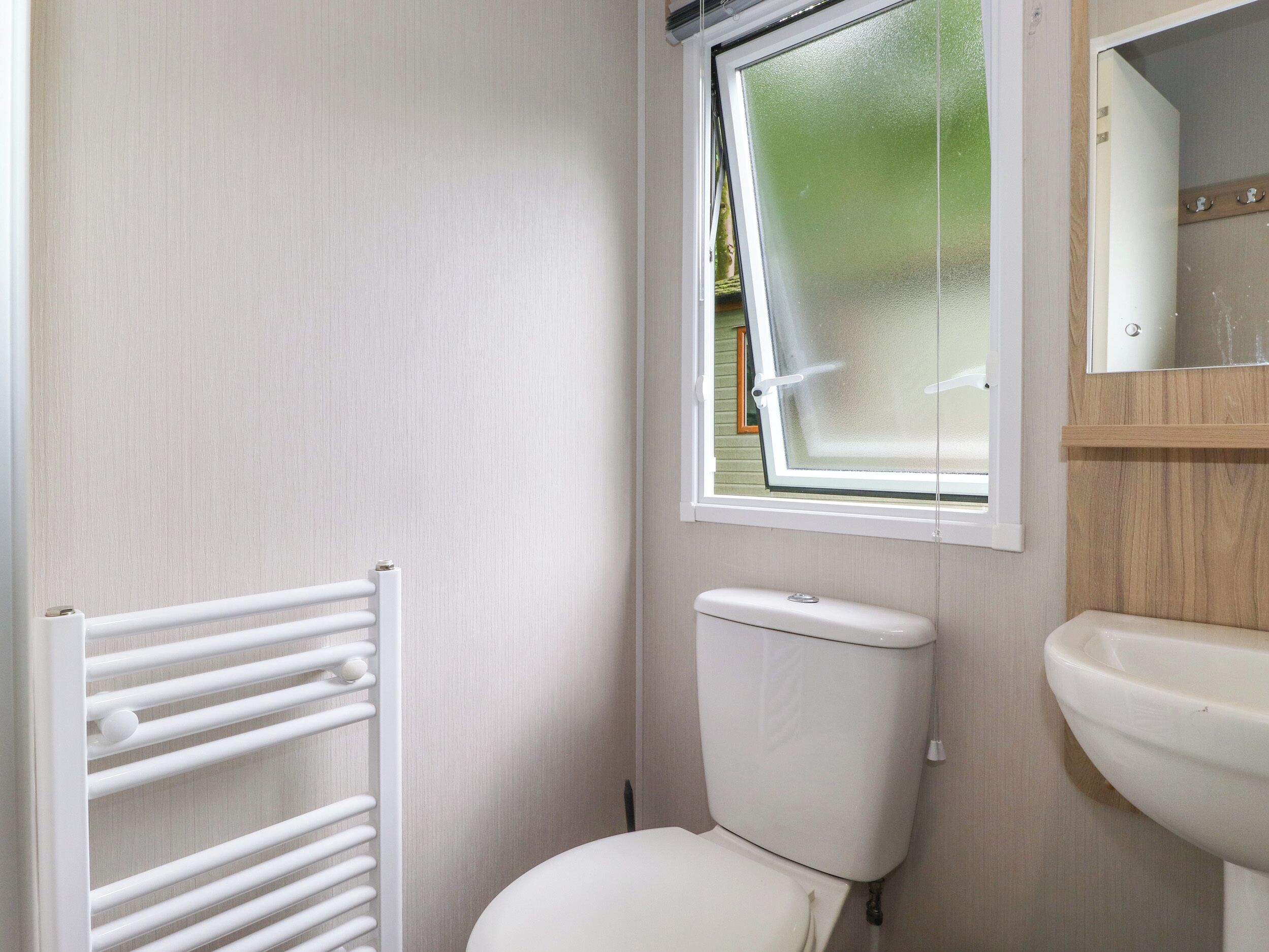 Een kleine badkamer met toilet, raam, radiator en wastafel.