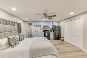 A bedroom with a bed, a ceiling fan, and a view into a kitchen with cabinets and appliances. - Private Yard: Pet-friendly Studio in New Boston! (New Boston)
