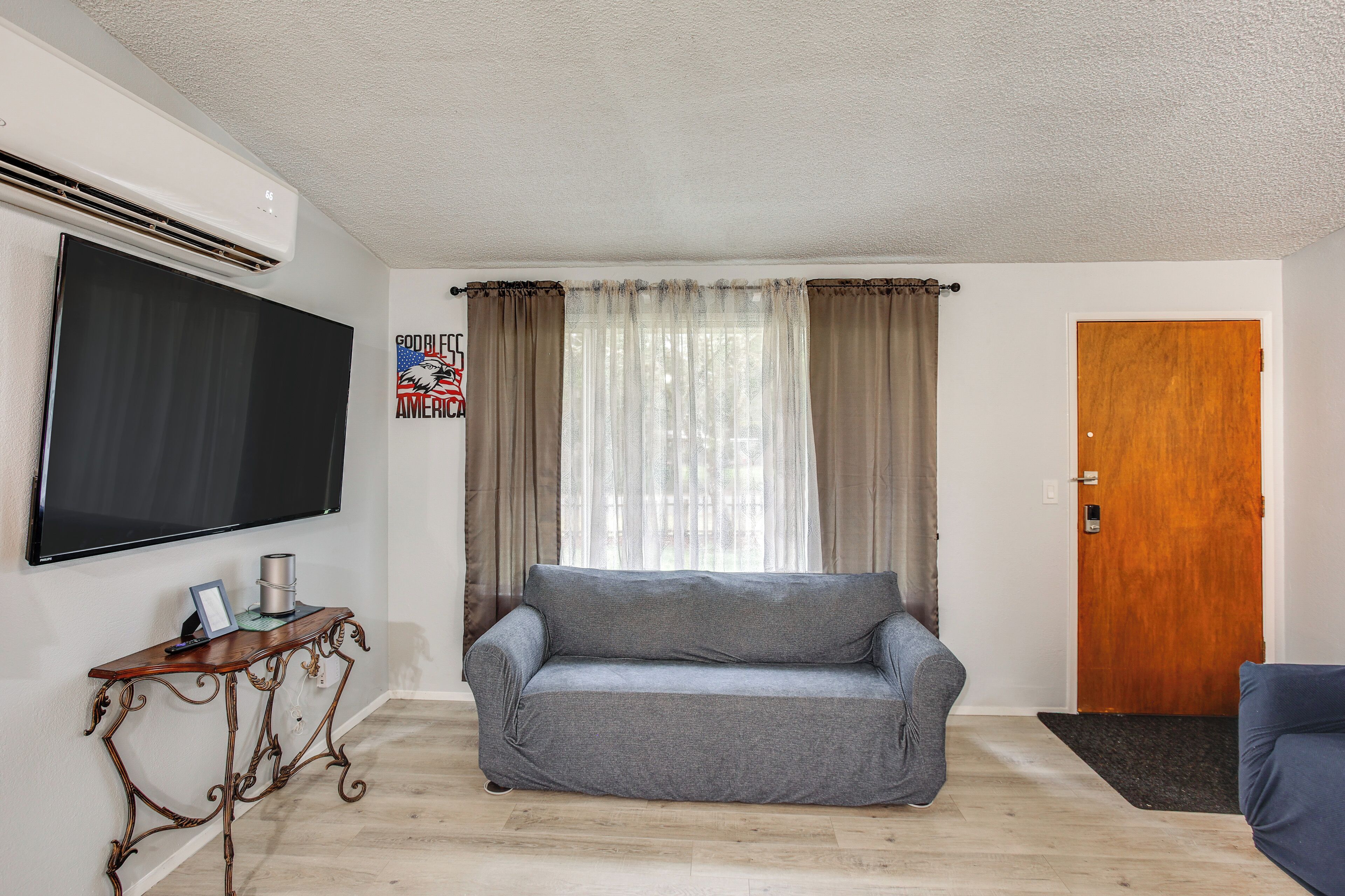 A living room with a grey sofa, a wooden console table, a flat-screen TV, and a wooden door.