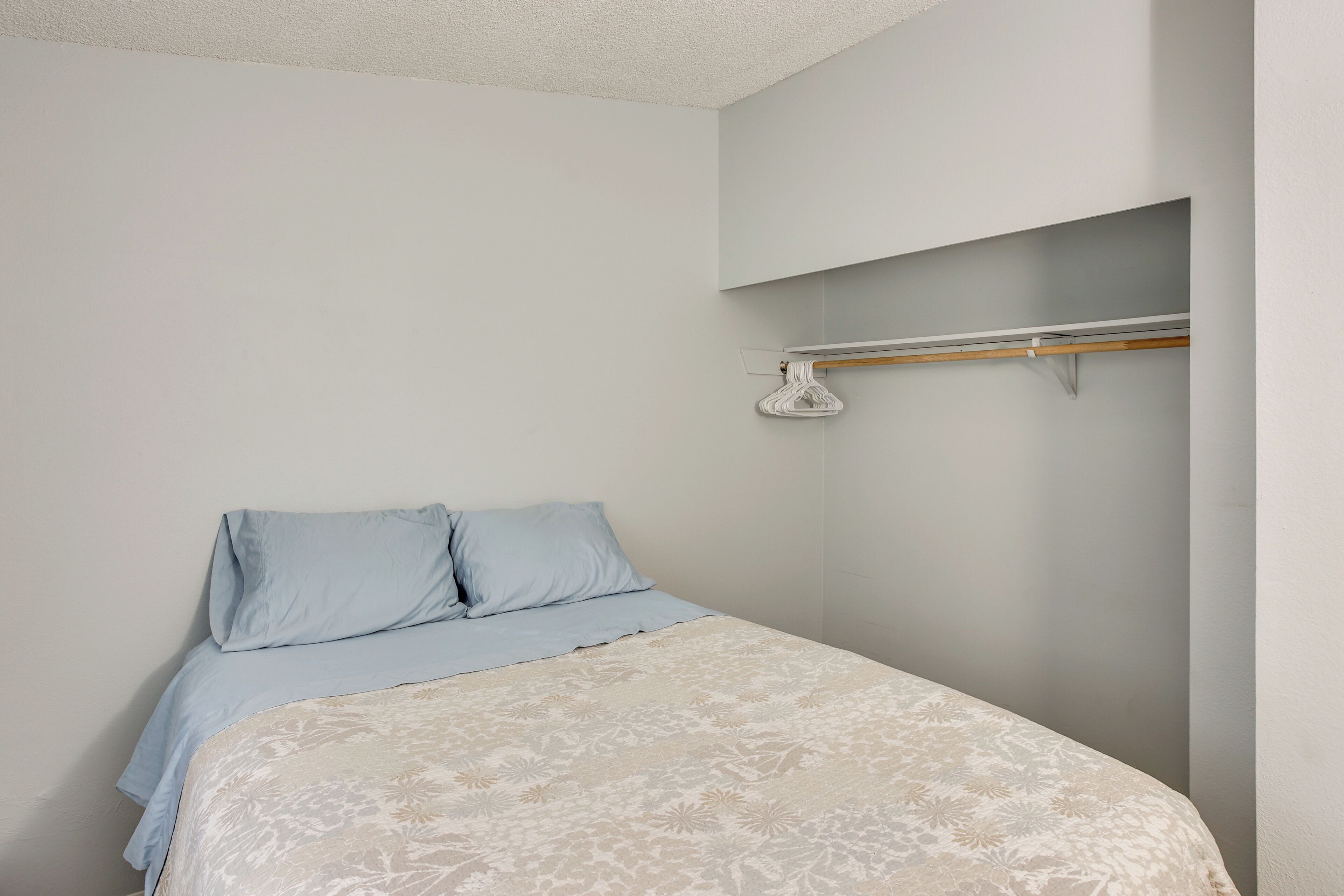 A bedroom with a bed, two pillows, a hanging coat rack, and a light-colored wall.
