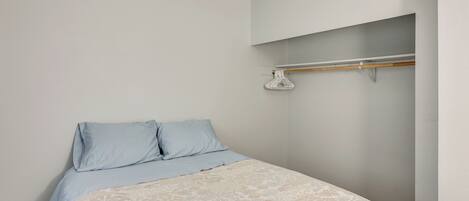 A bedroom with a bed, two pillows, a hanging coat rack, and a light-colored wall.