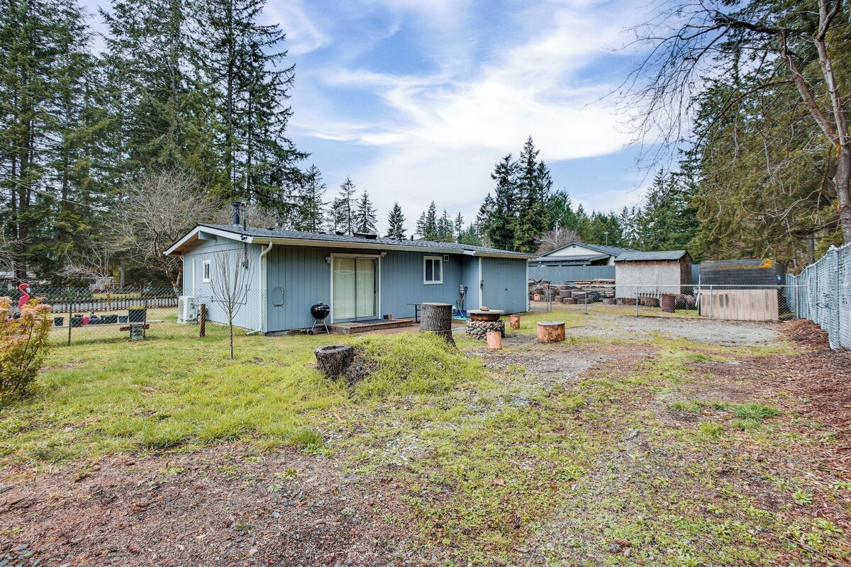 Eine kleine, eingeschossige Holzhütte mit Veranda, umgeben von einem eingezäunten Garten und dichtem Wald.