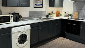 A modern kitchen with dark cabinets, a marble countertop, a washing machine, and a coffee machine. - Modern 1-bed Apartment - Sleeps 4 & Central Links (Birkenhead)