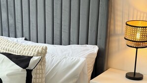 A neatly made bed with white bedding and decorative pillows, a bedside lamp, and a small plant on a nightstand. - Modern 1-bed Apartment - Sleeps 4 & Central Links (Birkenhead)