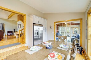 Een eethoek met een houten tafel, stoelen, een koelkast en uitzicht op de omgeving.
