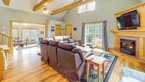 A spacious living room with a large leather sofa, a fireplace, and a television mounted on a wooden wall. - Dog Friendly Mountain View Retreat w/ Hot Tub (Purlear)