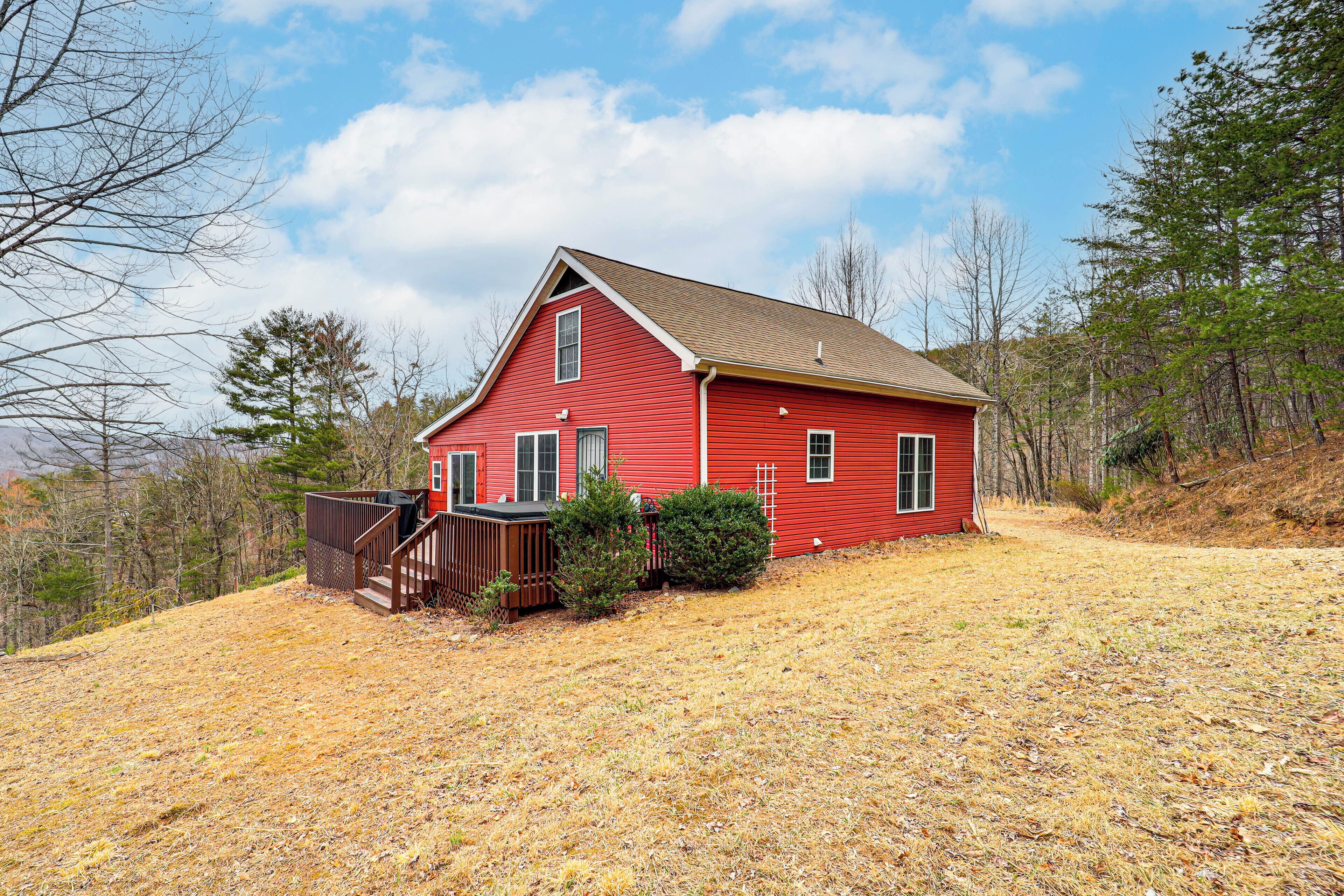 A red house with a brown deck, surrounded by dry grass and trees.