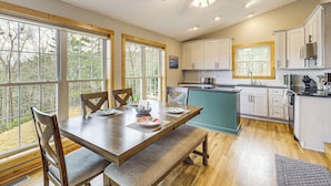 A spacious kitchen with wooden cabinets, a dining table with chairs, and large windows offering a view of the outdoors. - Dog Friendly Mountain View Retreat w/ Hot Tub (Purlear)