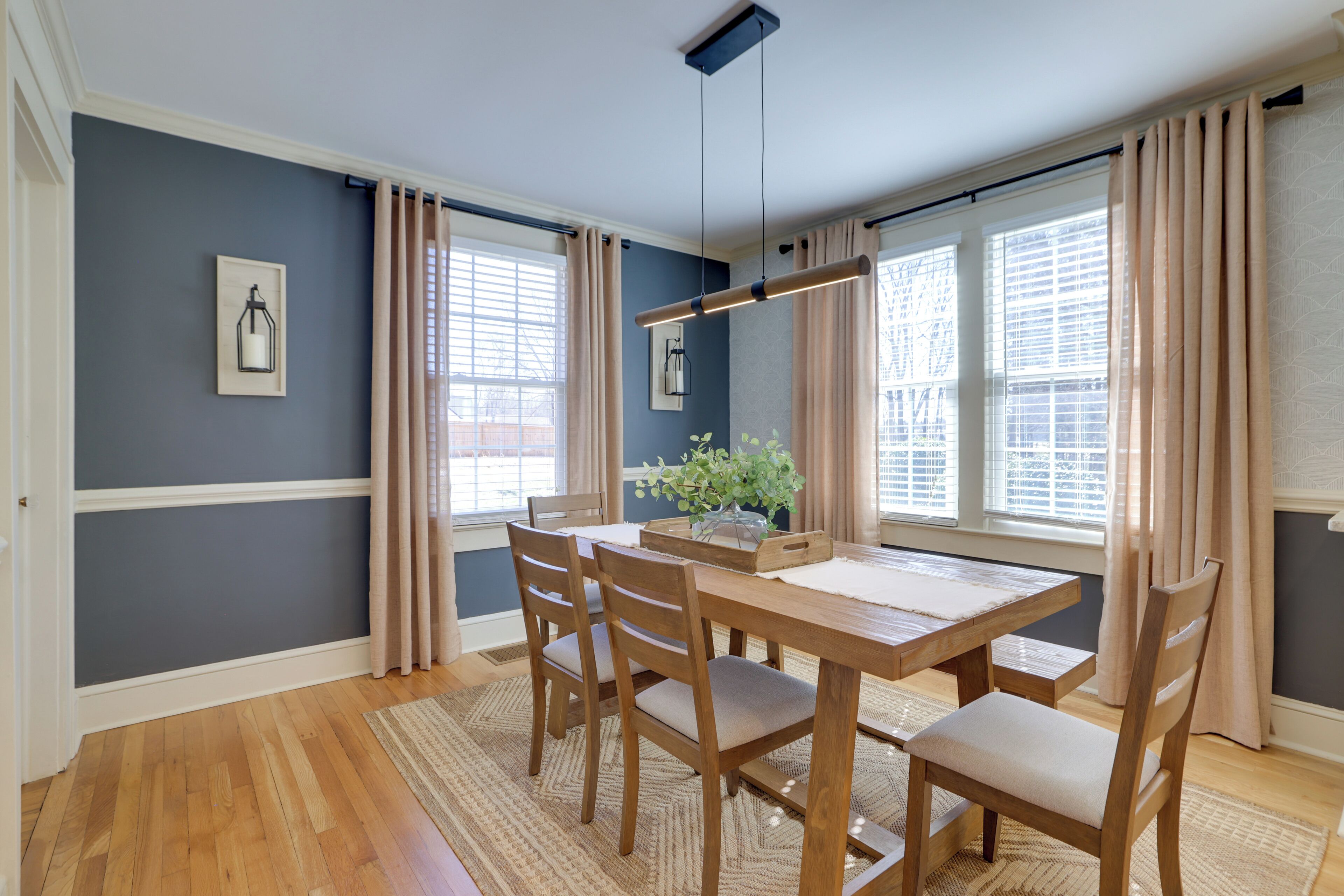 Un coin repas avec une table et des chaises en bois, un tapis et une plante posée sur le rebord de la fenêtre.