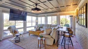 Un salón con ventanales, un sofá modular, una mesa de comedor y un televisor instalado en el techo.