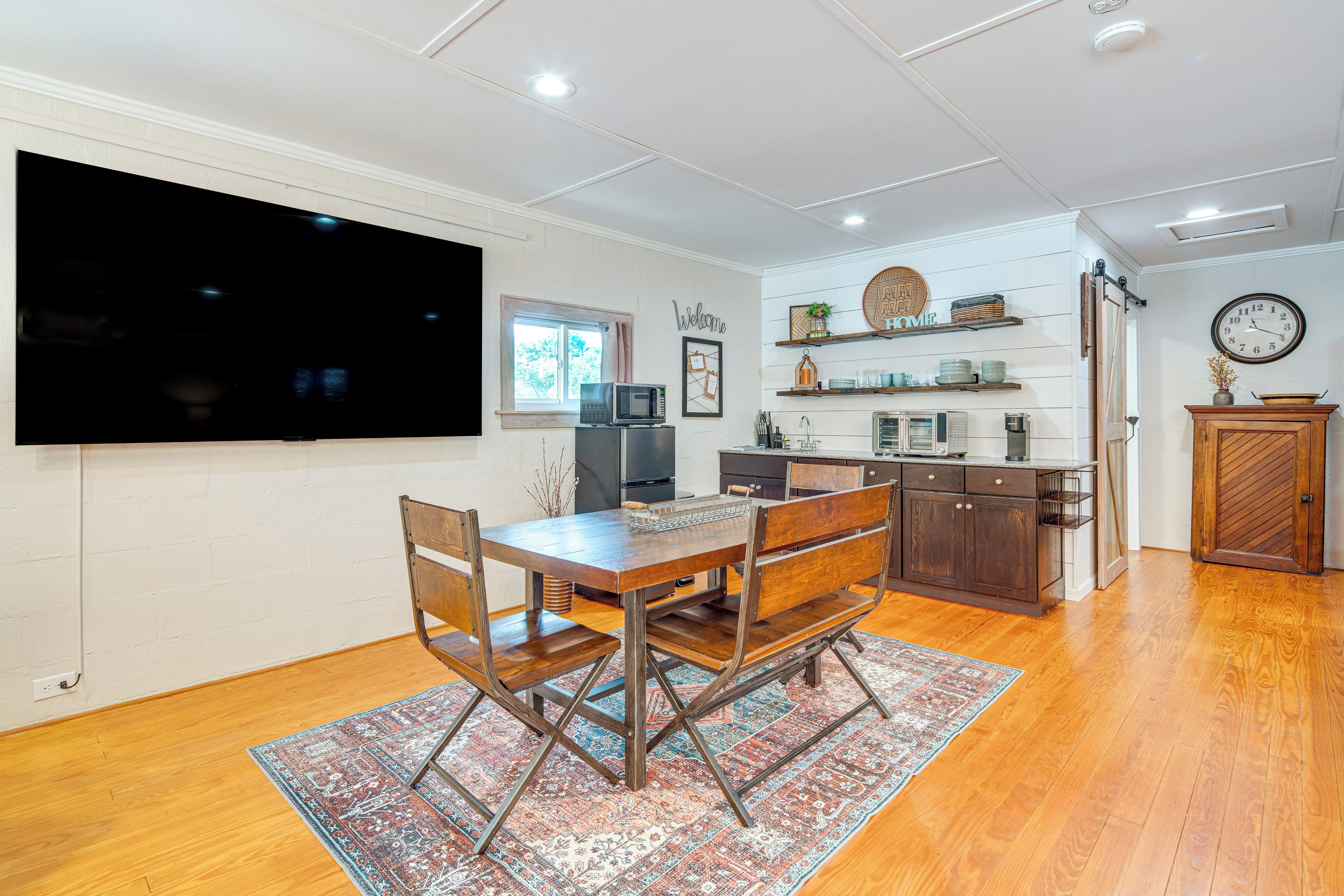 A modern kitchen with wooden cabinetry, a large flat-screen TV, and a dining area with a wooden table and chairs.