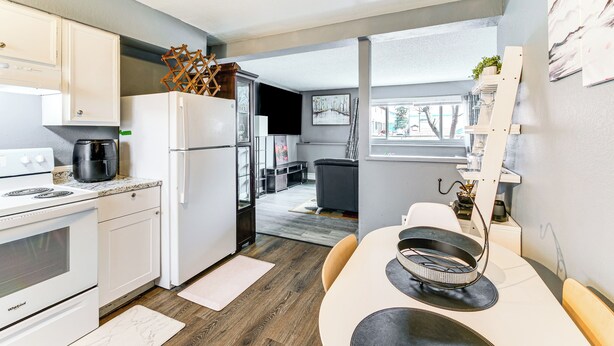 A compact kitchen with white appliances, a dining area with a round table, and a view into the living area. - 11 Mi to Kincaid Park: Convenient + Cozy Apt! (Anchorage)