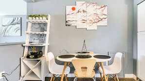 A dining area with a round table, white chairs, and a white shelving unit with glassware. - 11 Mi to Kincaid Park: Convenient + Cozy Apt! (Anchorage)