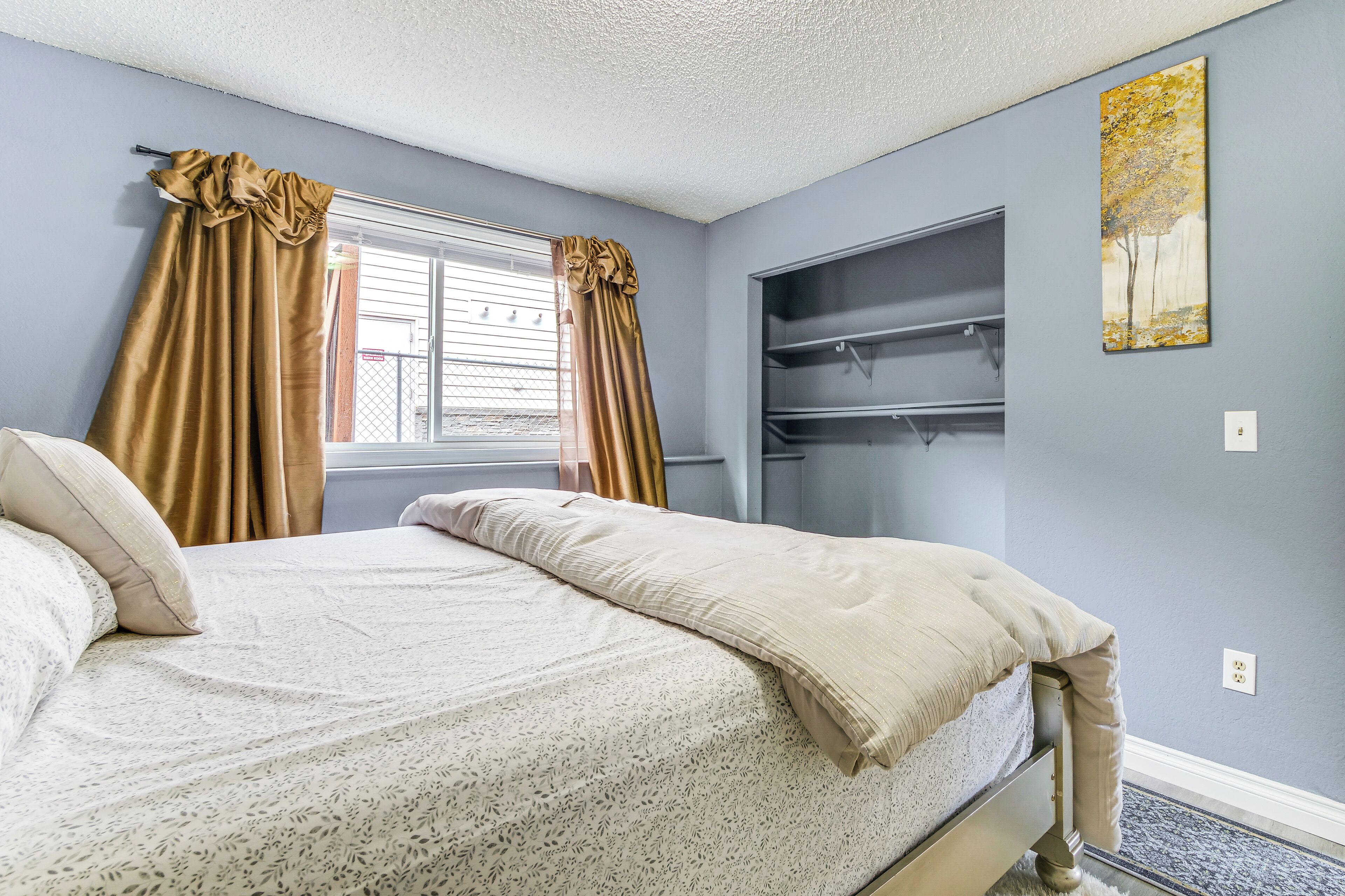 A bedroom with a bed, a window with curtains, a wardrobe, and a wall-mounted shelf.