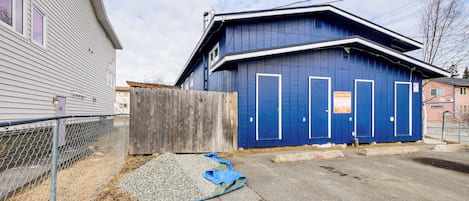 En bostadsbyggnad med en blå fasad, ett trästaket och en grusbelagd yta med en blå presenning.