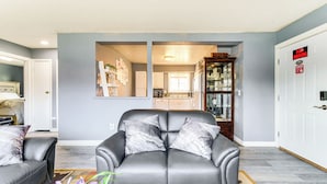 A living room with a black leather sofa, a coffee table, and a rug. There is a dining area visible through an open doorway. - 11 Mi to Kincaid Park: Convenient + Cozy Apt! (Anchorage)