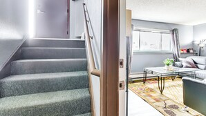 A staircase leading to a living area with a sofa, coffee table, and a window with curtains. - 11 Mi to Kincaid Park: Convenient + Cozy Apt! (Anchorage)