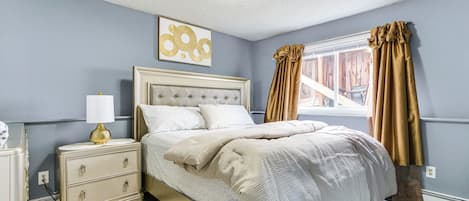 Un dormitorio con cama, mesita de noche, lámpara y una ventana con cortinas.
