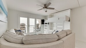 A modern living room with a curved sofa, a ceiling fan, and a large window with a view of the outdoors. - Dogs Welcome: Beachfront South Padre Island Condo (South Padre Island)