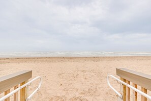 A wooden bench with metal handrails on a sandy beach with the ocean in the background. - Dogs Welcome: Beachfront South Padre Island Condo (South Padre Island)