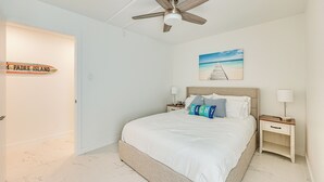 A bedroom with a bed, nightstands, a ceiling fan, a painting of a beach, and a sign on the wall. - Dogs Welcome: Beachfront South Padre Island Condo (South Padre Island)